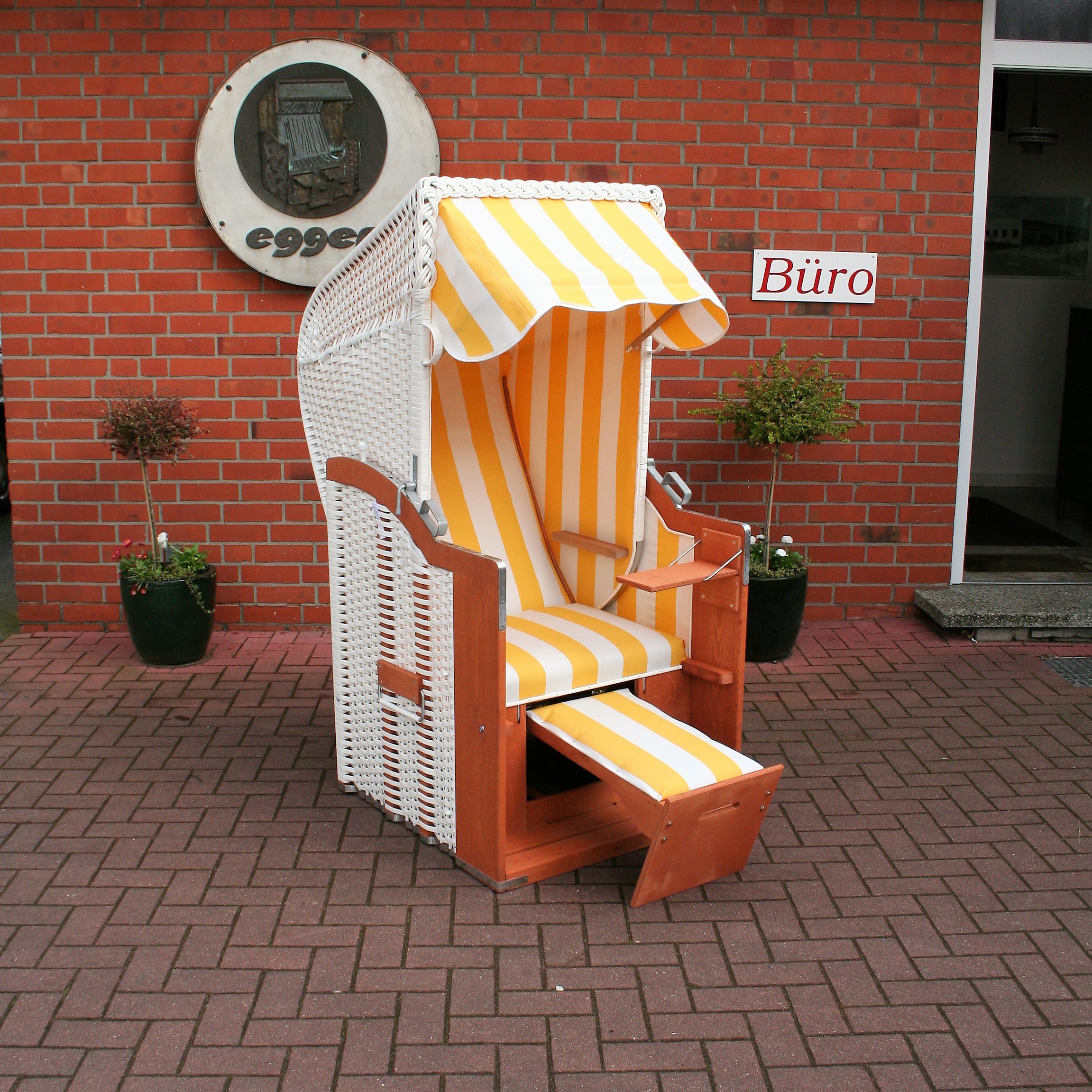 Der 1-Sitzer Strandkorb hat ein Geflecht aus PVC in der Farbe weiß mit einem gestreiften Stoffdesign in gelb-weiß.