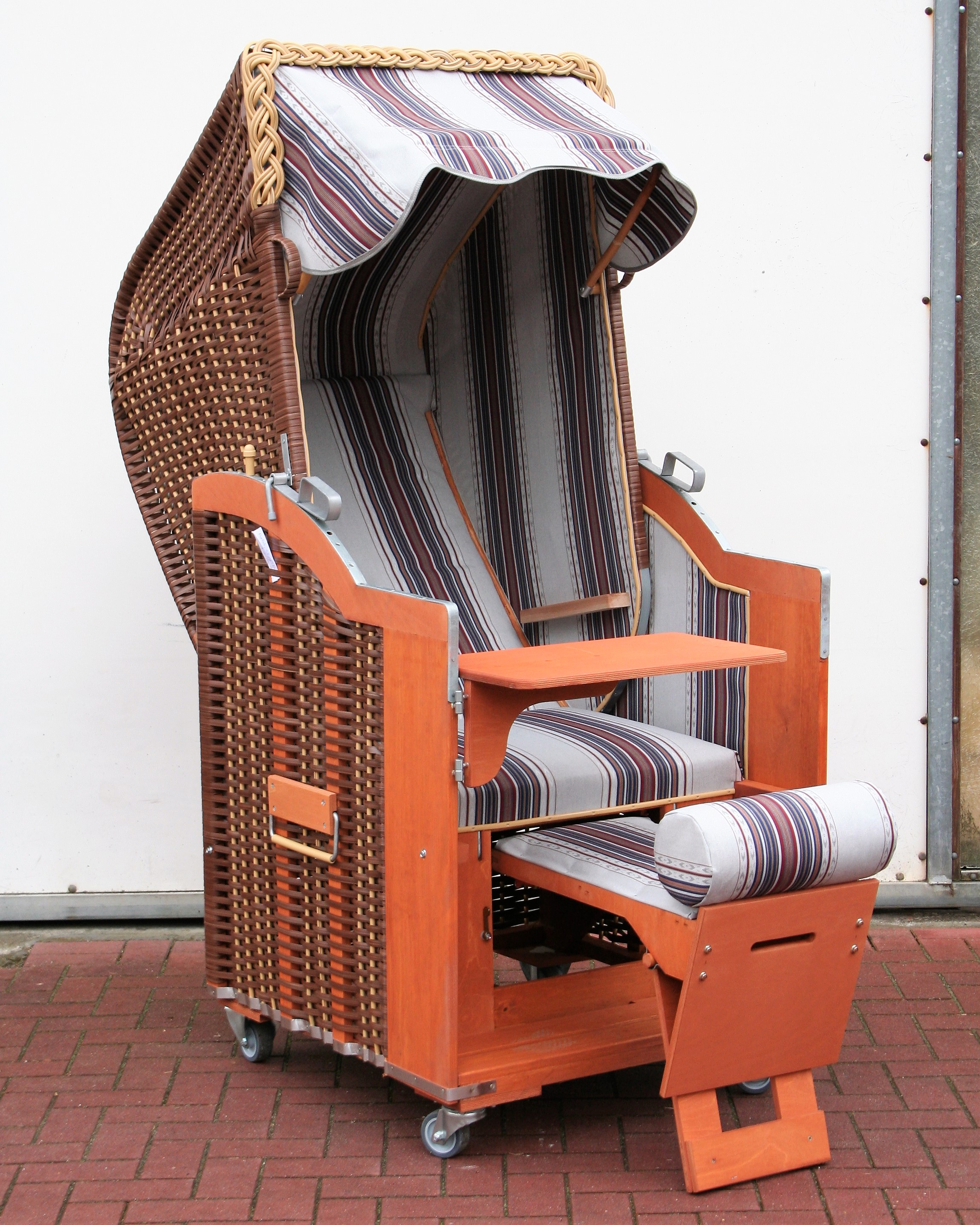 Der 1-Sitzer Strandkorb hat ein Geflecht aus PE in der Farbe braun/beige mit einem gestreiften Stoffdesign in grau-blau-bordeaux.